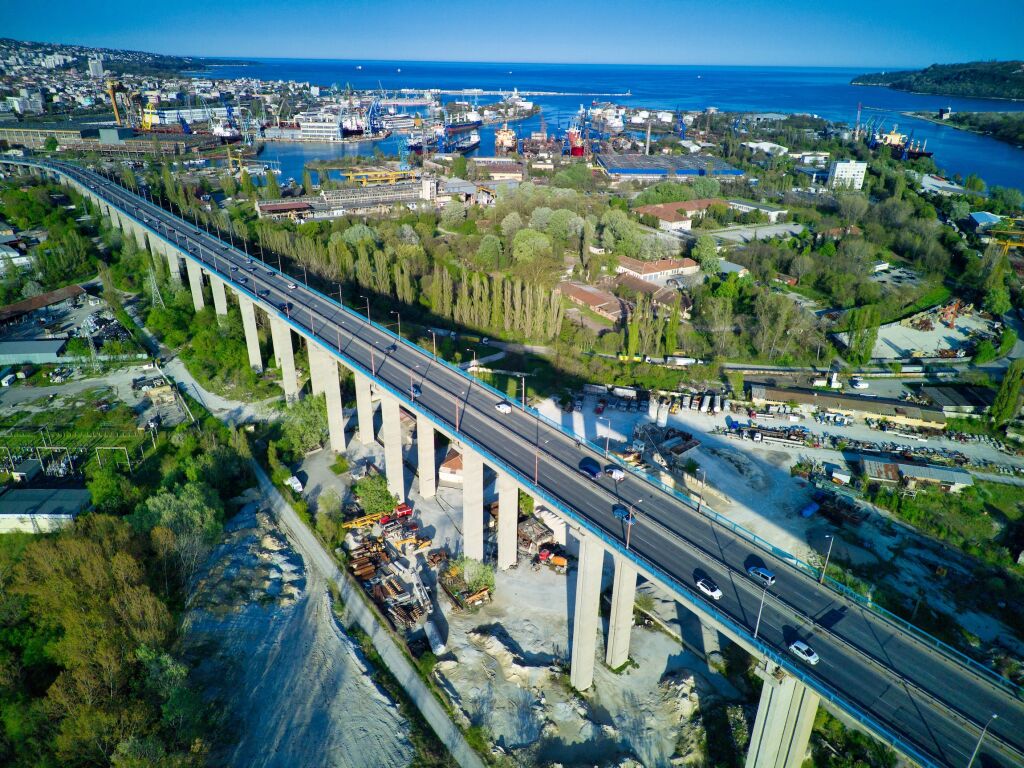 Widok z lotu ptaka na betonowy solidny most drogowy łączący tereny nowoczesnej infrastruktury nadmorskiego miasta Sozopol z wielopiętrowymi architektonicznymi domami wypoczynkowymi, w pobliżu głęboko niebieskiego falistego Morza Czarnego