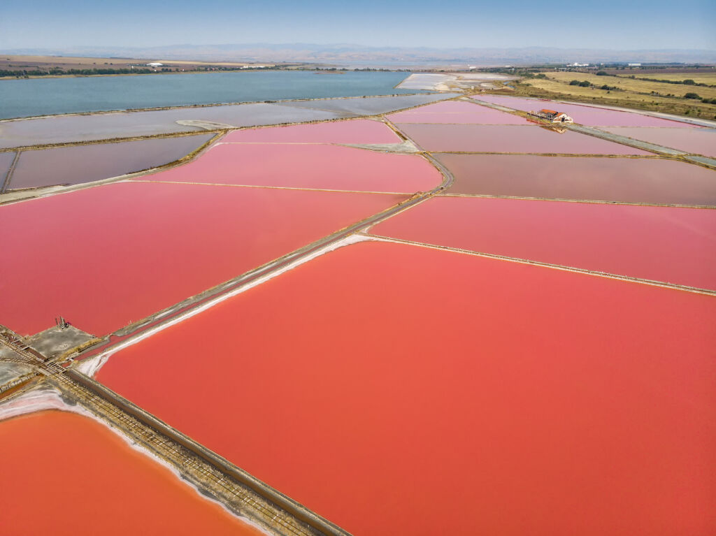 Burgas pink salt pans near Black sea aerial drone view. Jezioro dostarcza leczniczego błota i ługu. Jego niesamowity kolor pochodzi od mikroskopijnych krewetek solankowych i wodorostów, a także soli magnezowej w wodzie.