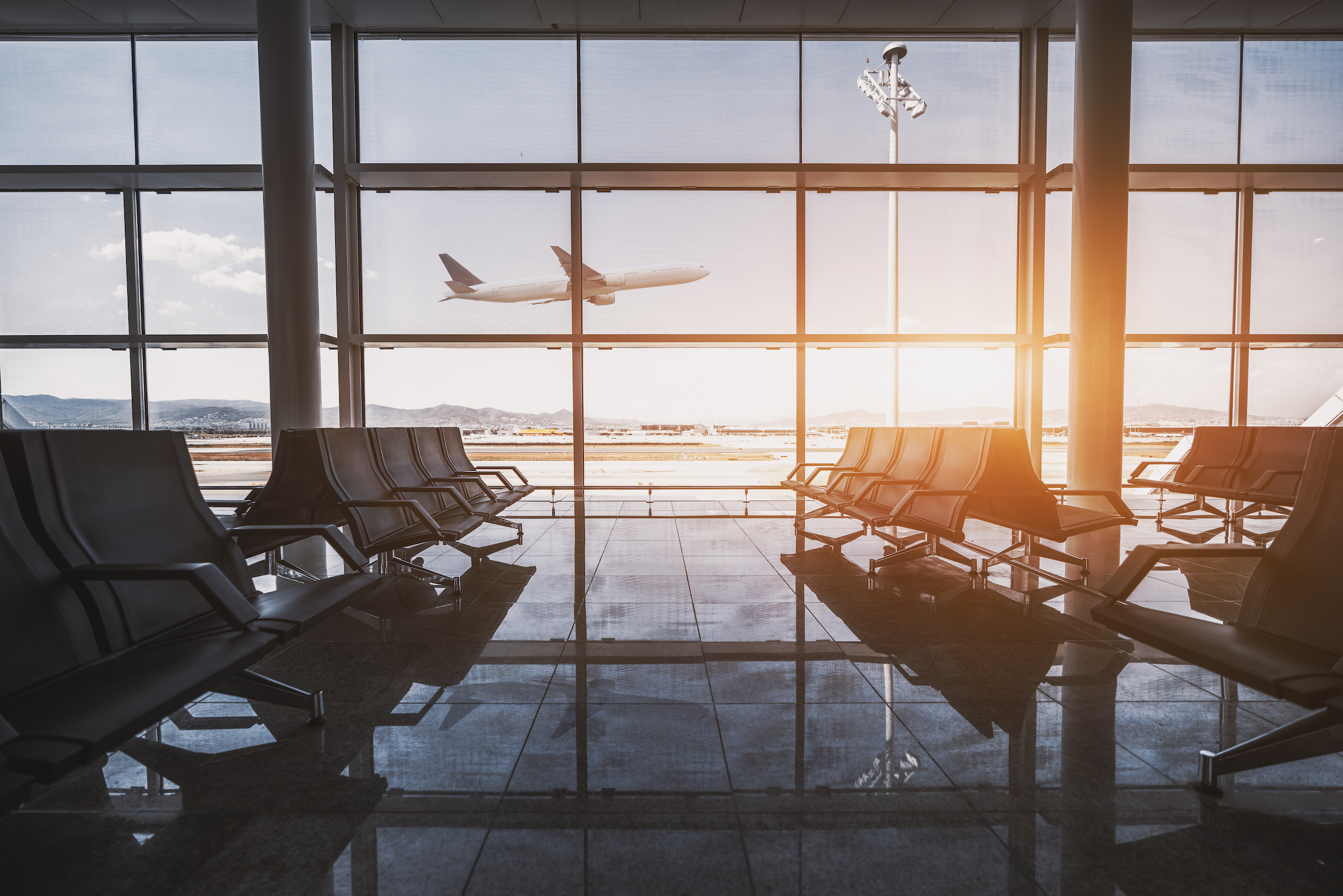Szerokokątny widok nowoczesnego samolotu zyskującego wysokość poza szklaną fasadą okna współczesnej poczekalni z wieloma rzędami siedzeń i odbicia wewnątrz terminalu lotniskowego