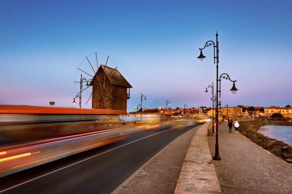 Stary wiatrak w starożytnym mieście Nesebar w Bułgarii.Wejście do starego miasta. Bułgarskie wybrzeże Morza Czarnego. Miejsce światowego dziedzictwa UNESCO. Droga, nocne światła. Ścieżki świetlne samochodów. Długa ekspozycja