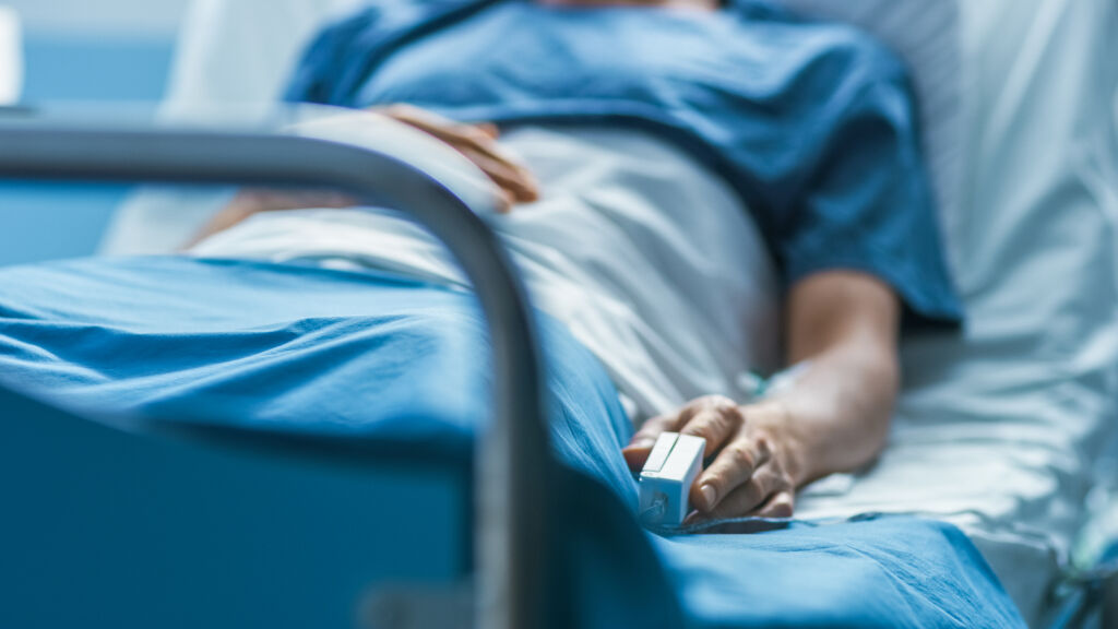 Szpitale w Słonecznym Brzegu - W szpitalu chory męski pacjent śpi na łóżku. Sprzęt monitorujący tętno jest na jego palcu.