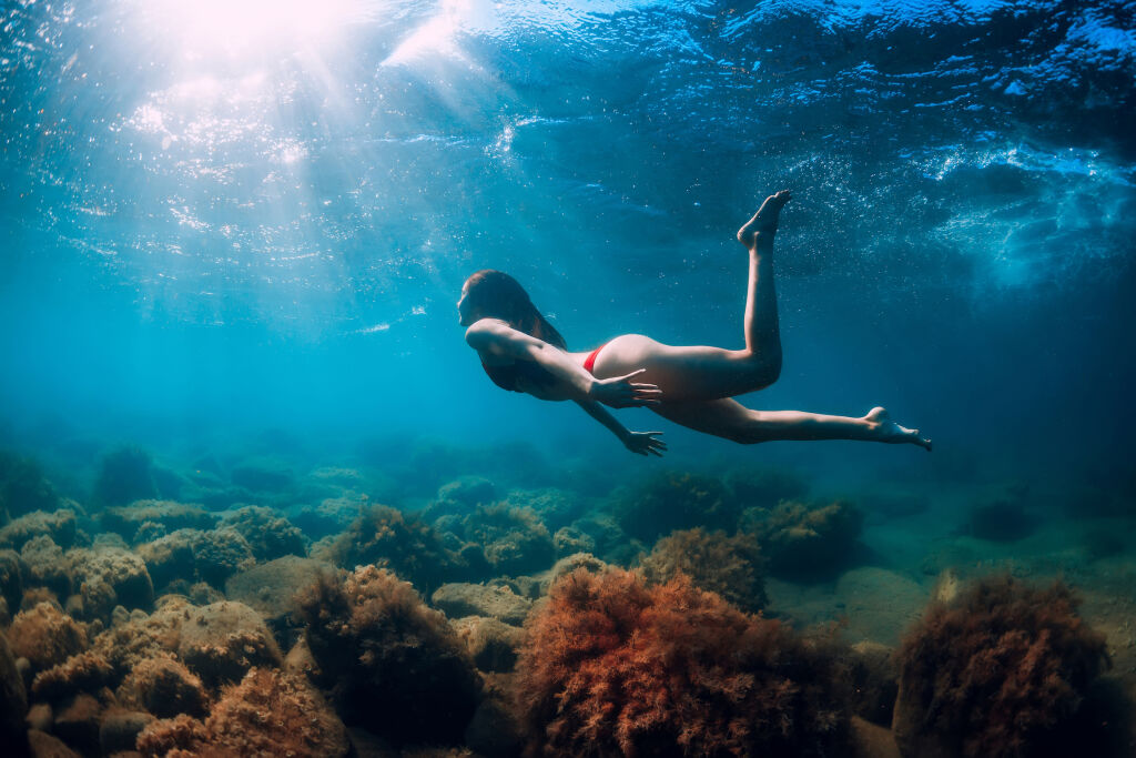 Młoda kobieta pływać i nurkować pod wodą w niebieskim morzu. Aktywność letnie dni na morzu - TOP 15 atrakcji na udane wakacje w Słonecznym Brzegu