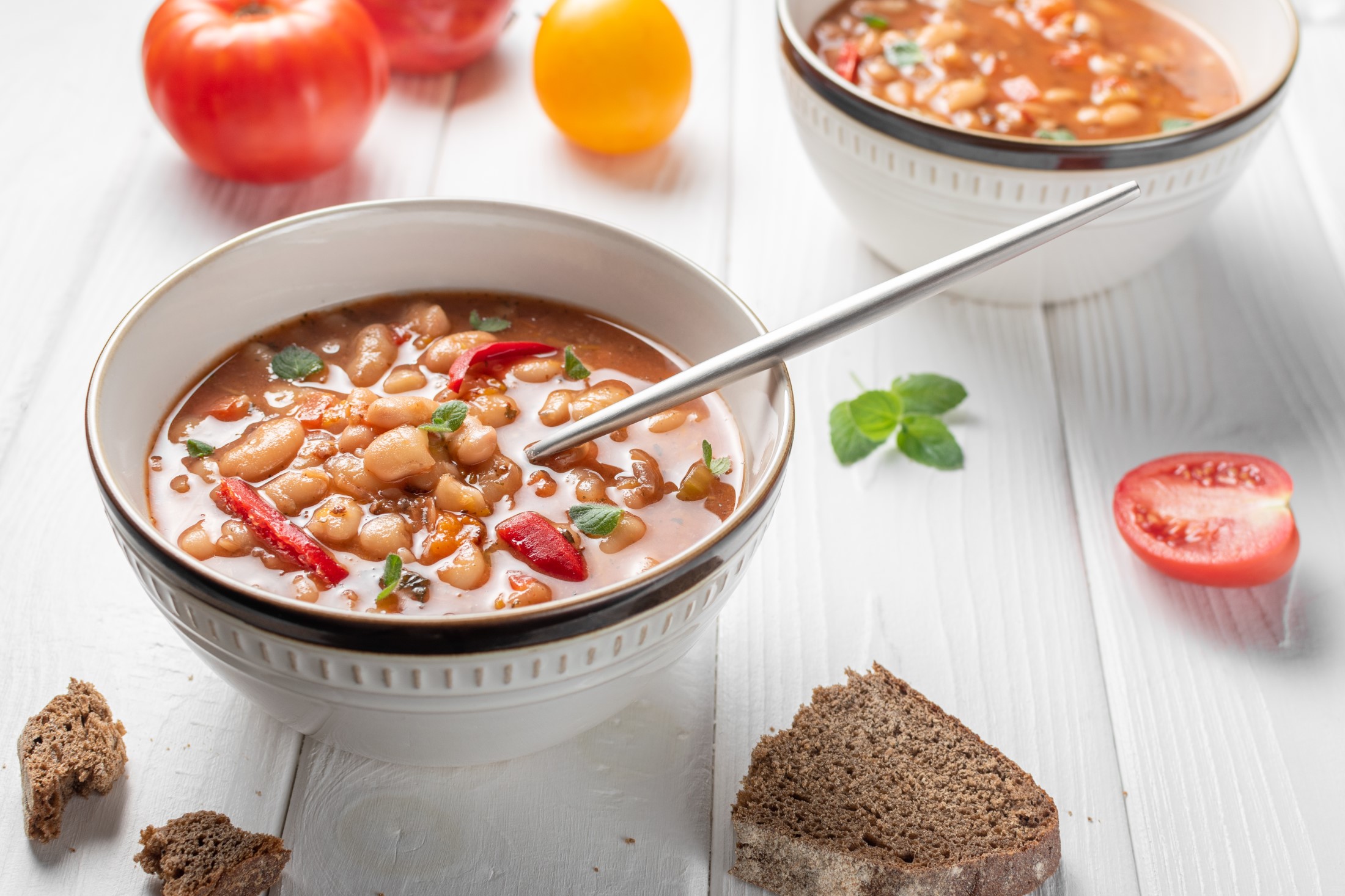Bulgarian Bean Soup - Bob Chorba, tomatoes, bread and mint on white wooden table. Horizontal orientation.